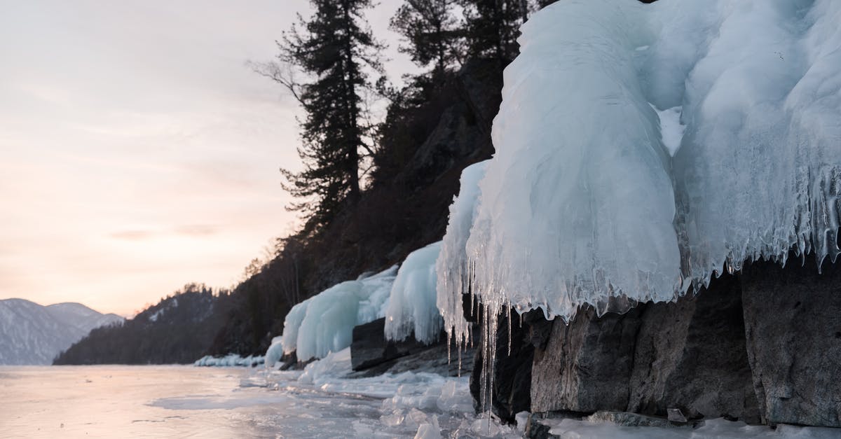 Thick carbon layer on wok? - Icicles on hillside near frozen lake under cloudy sky Thick carbon layer on wok? - Icicles on hillside near frozen lake under cloudy sky