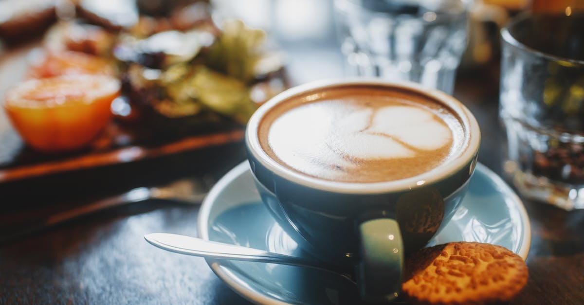 Thickening almond milk in hot liquids - Cup of cappuccino with delicate foam and pattern on saucer next to cookie and teaspoon on wooden table Thickening almond milk in hot liquids - Cup of cappuccino with delicate foam and pattern on saucer next to cookie and teaspoon on wooden table