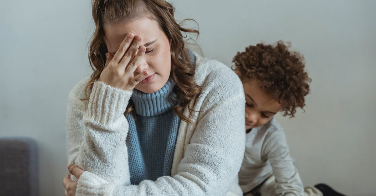 Timing problem! [duplicate] - Frustrated mother with hand on forehead and closed eyes sitting near African American son near wall in room at home