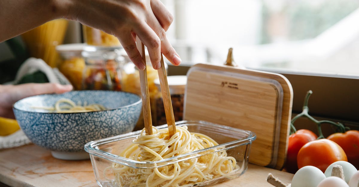 Tomato Products containing Citric Acid - Unrecognizable female cook with tongs standing at counter with glass container of fresh pasta while cooking in kitchen on blurred background Tomato Products containing Citric Acid - Unrecognizable female cook with tongs standing at counter with glass container of fresh pasta while cooking in kitchen on blurred background