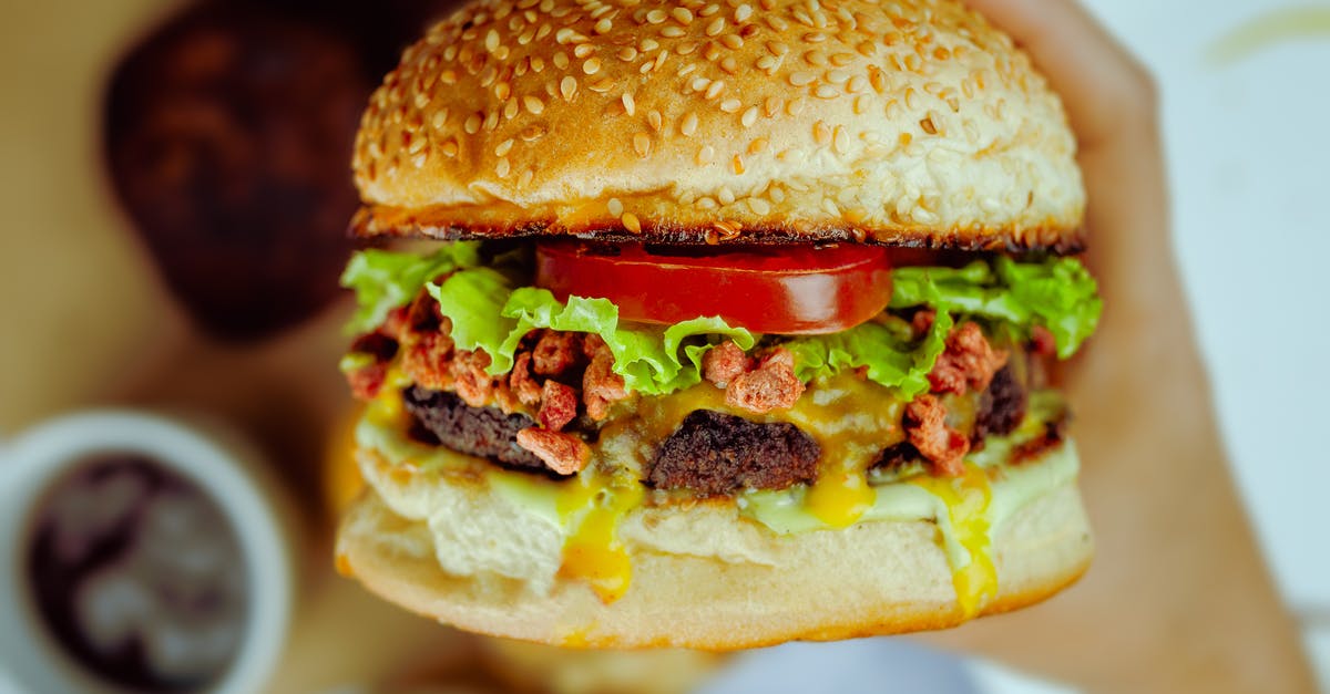 Tomato Sauce Turns Dark/Sweet - Unrecognizable person eating big delicious hamburger with dark brown cutlet and fresh vegetable between buns covered with edible seeds Tomato Sauce Turns Dark/Sweet - Unrecognizable person eating big delicious hamburger with dark brown cutlet and fresh vegetable between buns covered with edible seeds