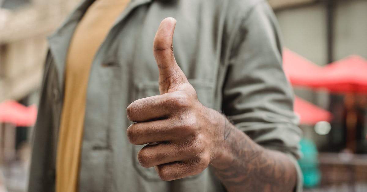 TV Programs like Good Eats - Crop faceless young black male in casual outfit standing on city street and showing thumb up gesture TV Programs like Good Eats - Crop faceless young black male in casual outfit standing on city street and showing thumb up gesture