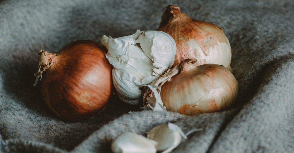 Unpeeled garlic cloves in French / Belgian cooking? - High angle of unpeeled golden onions and garlic bulb placed on soft plaid in kitchen Unpeeled garlic cloves in French / Belgian cooking? - High angle of unpeeled golden onions and garlic bulb placed on soft plaid in kitchen