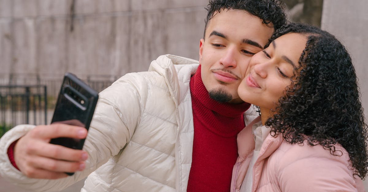 Use by date on cacao butter - Enamored young Hispanic couple in warm casual clothes smiling and touching cheeks while taking selfie on mobile phone standing on street Use by date on cacao butter - Enamored young Hispanic couple in warm casual clothes smiling and touching cheeks while taking selfie on mobile phone standing on street