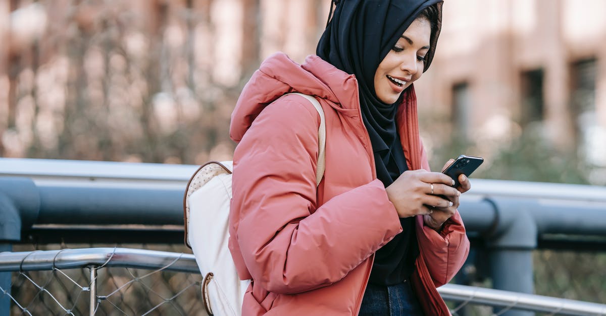 Using cast iron pans only - Muslim ethnic female in hijab texting message on mobile phone near iron construction on blurred background of building Using cast iron pans only - Muslim ethnic female in hijab texting message on mobile phone near iron construction on blurred background of building