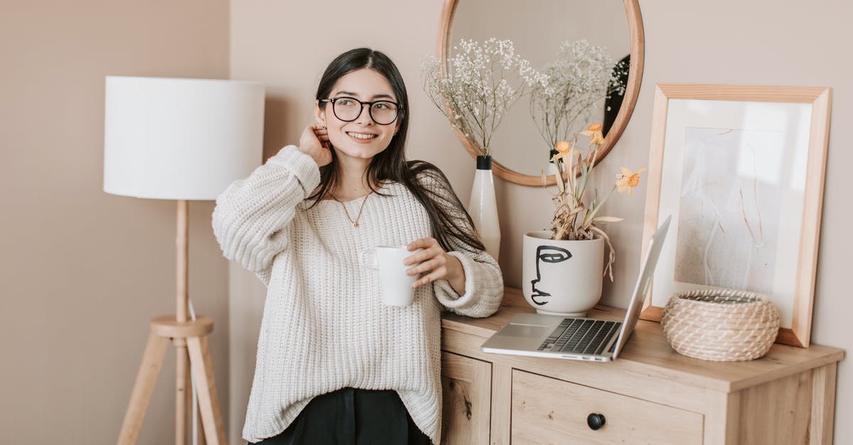 Using sous vide to warm canned vegetables - Dreamy smiling young lady in white sweater and eyeglasses with mug of hot beverage looking away happily while standing near bedroom dresser and browsing laptop Using sous vide to warm canned vegetables - Dreamy smiling young lady in white sweater and eyeglasses with mug of hot beverage looking away happily while standing near bedroom dresser and browsing laptop