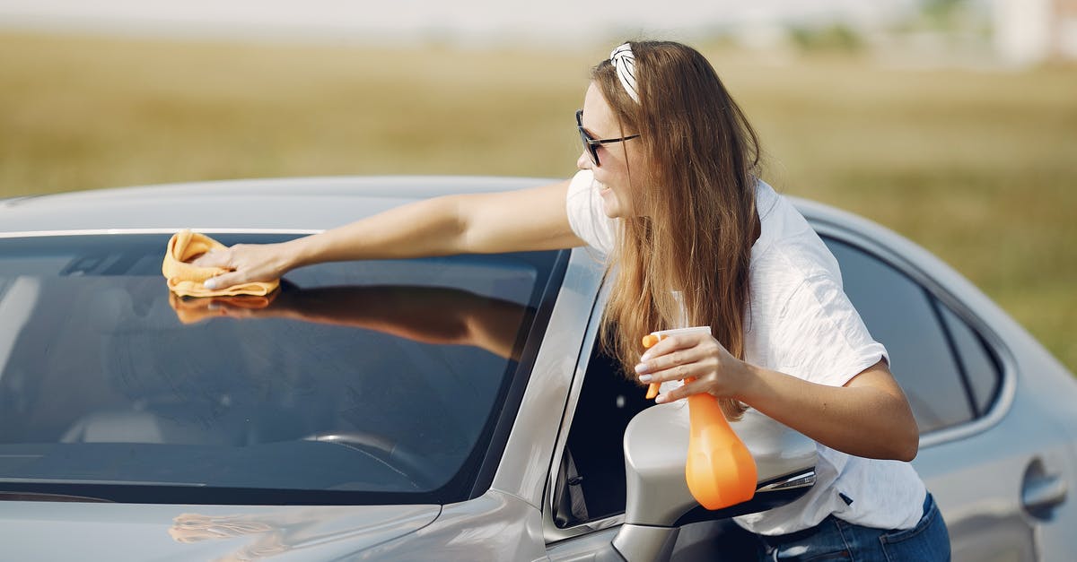 Washing Griddle before first use - Side view of cheerful female driver in sunglasses and casual clothes cleaning windshield of modern car with microfiber cloth and spray bottle against green field Washing Griddle before first use - Side view of cheerful female driver in sunglasses and casual clothes cleaning windshield of modern car with microfiber cloth and spray bottle against green field