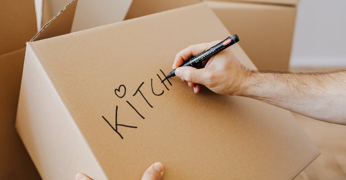 What's the black thing at the bottom of navel oranges? - From above of unrecognizable adult male writing with black marker on cardboard containers while packing staff and preparing for relocation in new home