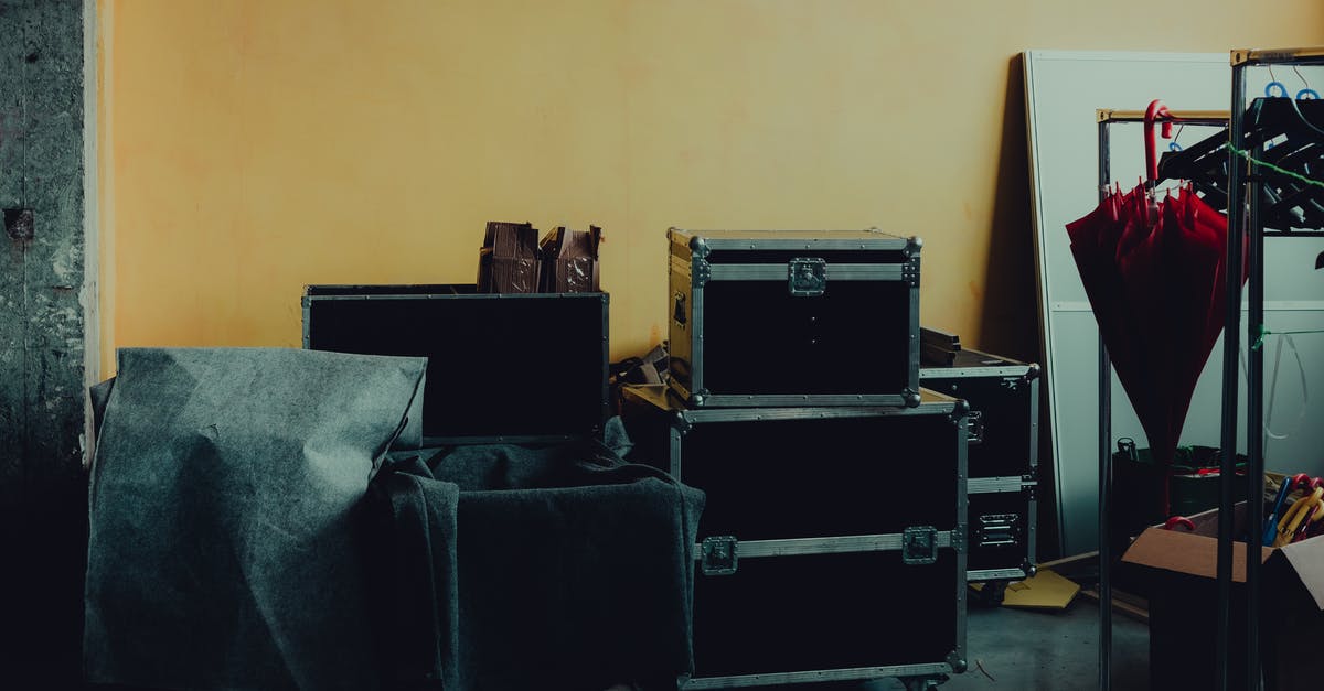What's the black thing at the bottom of navel oranges? - Many boxes and huge iron cases near umbrella placed in room with yellow walls