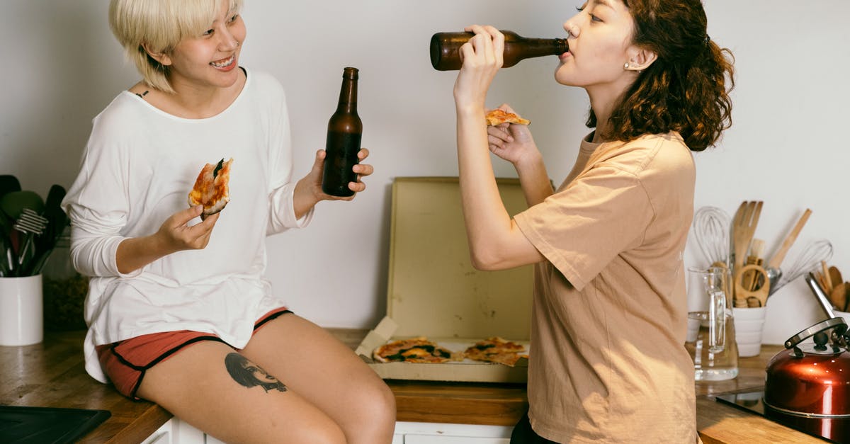 What are other uses for a pizza stone? - Happy tattooed blond lady eating pizza while looking at female friend in casual wear drinking beverage from bottle near kitchen utensils in apartment What are other uses for a pizza stone? - Happy tattooed blond lady eating pizza while looking at female friend in casual wear drinking beverage from bottle near kitchen utensils in apartment