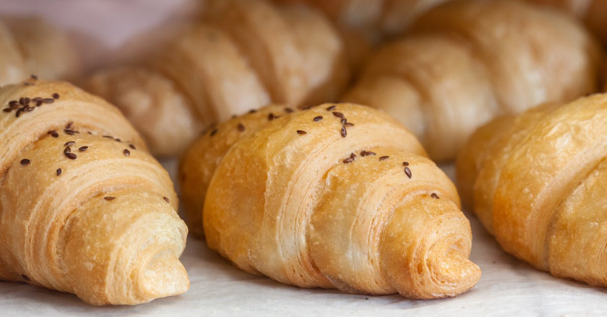 What causes a food to become tough as opposed to crispy or flaky when pan frying or baking? - Delicious baked croissants with little brown sesame seeds on top placed on white cloth in bakery