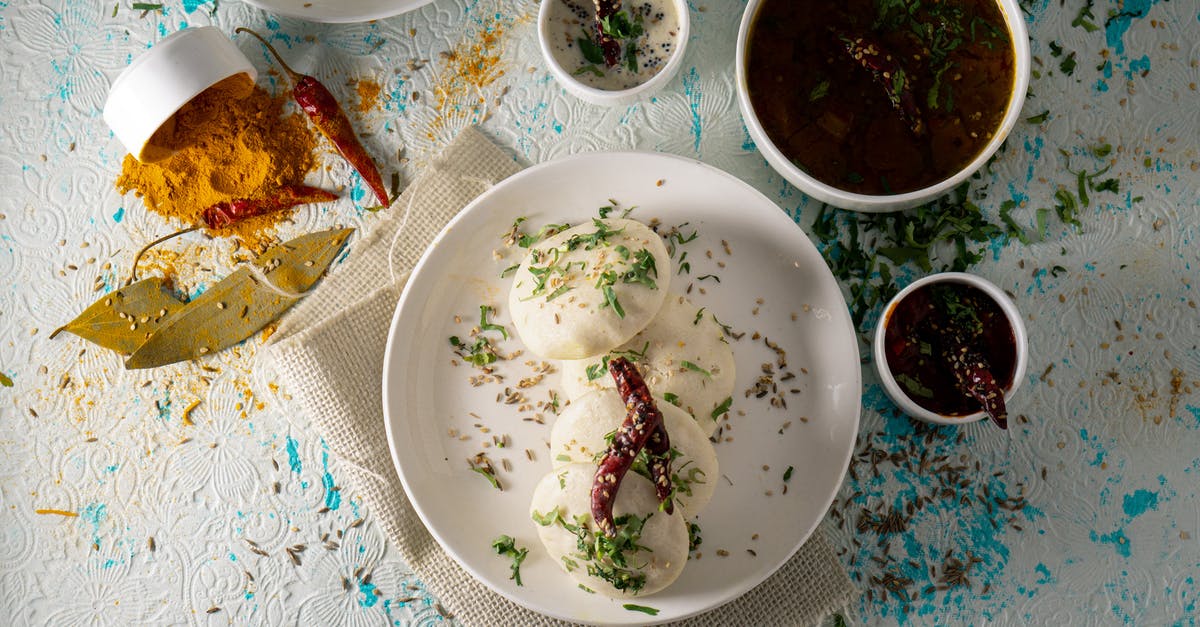 What determines spice level in Indian cuisine? - Top view of delicious Idli rice cakes with herbs and spicy tomato soup served on table near sauces and scattered spices