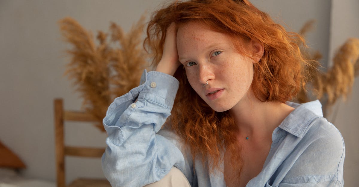 What does the ash content of broken wheat really mean? - Dreamy female with red hair looking at camera while leaning on hand in room with dry plant on blurred background
