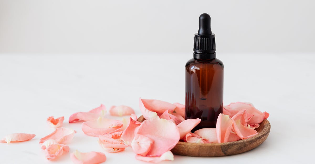 What exactly is essence? - Gentle pale pink wavy rose petals placed on small round wooden plate and table near dark glass essence flask on white background What exactly is essence? - Gentle pale pink wavy rose petals placed on small round wooden plate and table near dark glass essence flask on white background