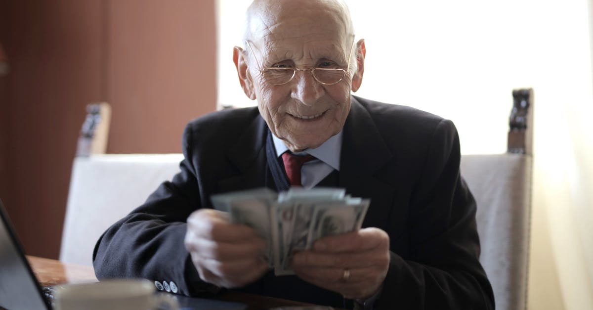 What factors lead to rich crema on espresso? - Positive senior businessman in formal suit and eyeglasses counting money bills while sitting at wooden table with cup of beverage and near opened laptop What factors lead to rich crema on espresso? - Positive senior businessman in formal suit and eyeglasses counting money bills while sitting at wooden table with cup of beverage and near opened laptop