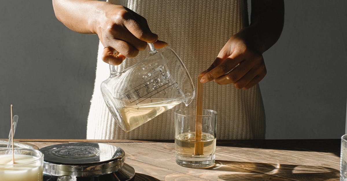 What happened to my melted couverture? - Unrecognizable African American female pouring melted wax from beaker into glass mold with wooden wick while making candles at table
