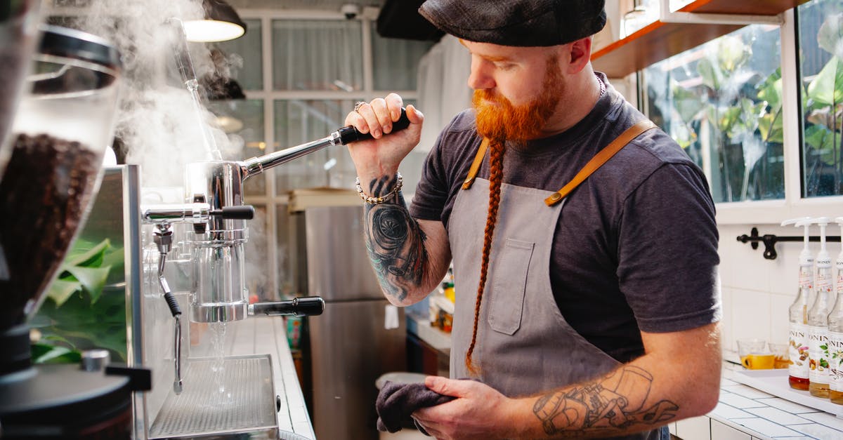What is a kitchen rag? - Tattooed barista cleaning coffee maker with steam What is a kitchen rag? - Tattooed barista cleaning coffee maker with steam