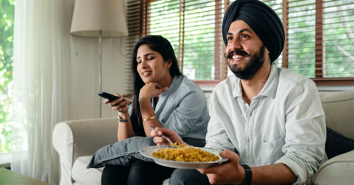 What is a suitable Low carb rice alternative? - Positive young bearded man in casual wear and turban eating traditional saffron rice on sofa while wife switching channels on TV with remote controller What is a suitable Low carb rice alternative? - Positive young bearded man in casual wear and turban eating traditional saffron rice on sofa while wife switching channels on TV with remote controller