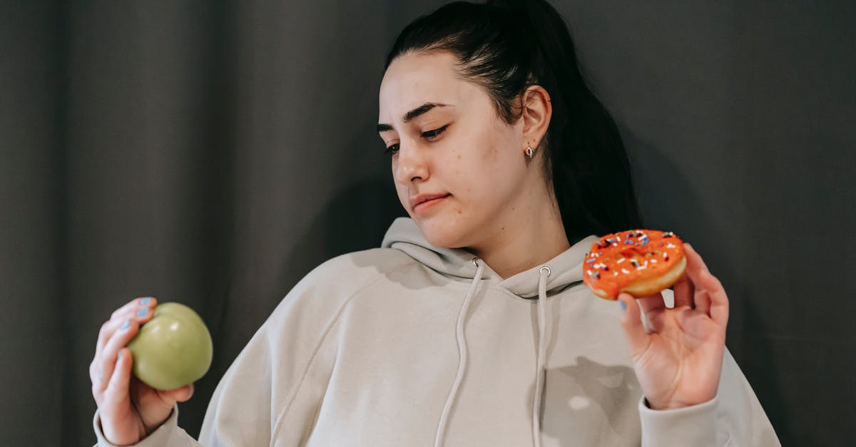 What is the difference between doughnut and krapfen? - Pensive female wearing casual hoodie deciding between healthy green apple and sweet doughnut in studio What is the difference between doughnut and krapfen? - Pensive female wearing casual hoodie deciding between healthy green apple and sweet doughnut in studio