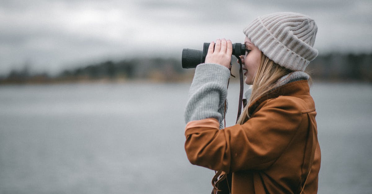 What is the difference between using hot water and cold water when making regular pastry? - Side view of female in warm clothes smiling and using binoculars on blurred background of embankment