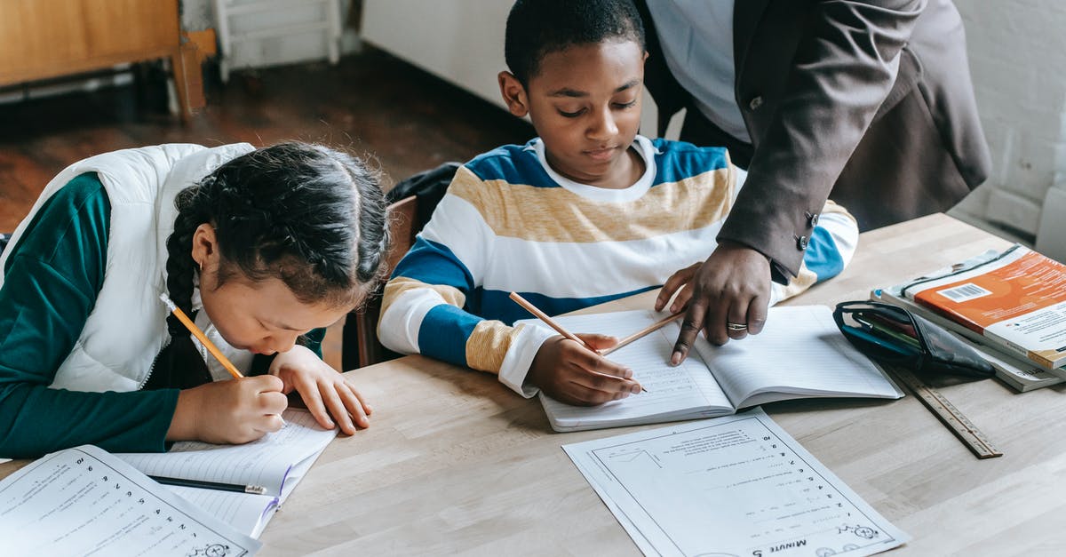 What is the point in combining sucralose and acesulfame potassium? - High angle of crop unrecognizable black female teacher explaining task to focused little schoolboy sitting at desk near attentive Asian classmate writing in notebook
