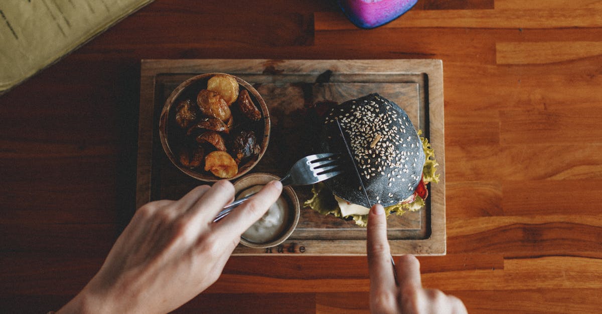 What is the point of mustard-frying burger patties? - Top view of crop anonymous person cutting appetizing black burger served on wooden board with sauce and fried potatoes What is the point of mustard-frying burger patties? - Top view of crop anonymous person cutting appetizing black burger served on wooden board with sauce and fried potatoes