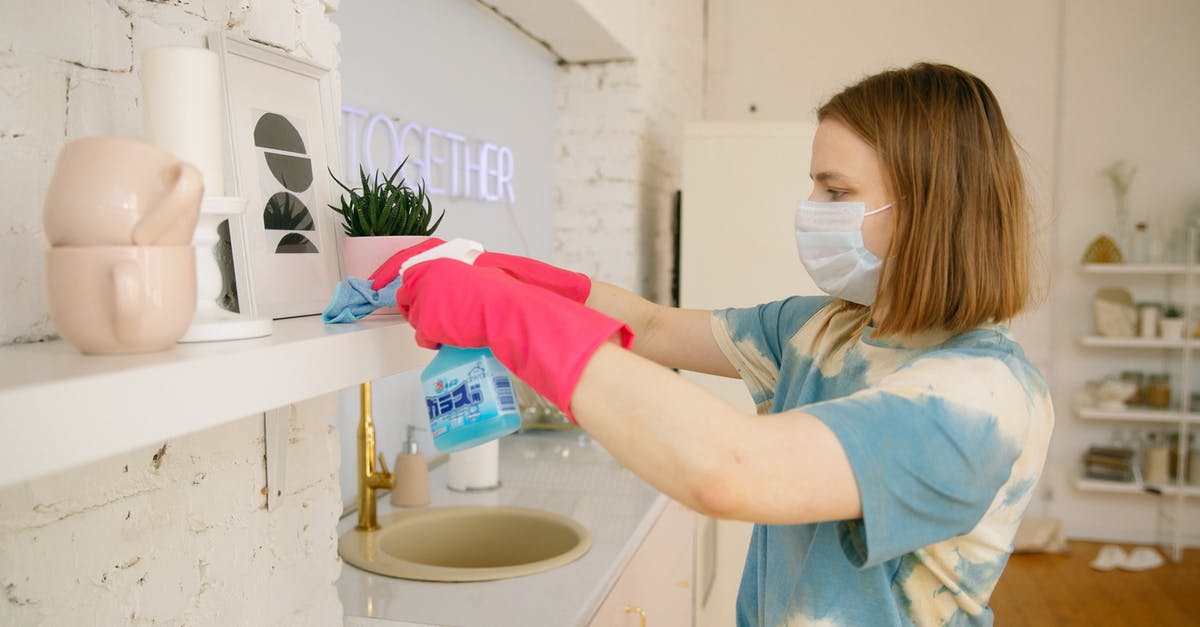 What is the preferred method for sanitizing the kitchen? - Woman Wearing Face Mask While Cleaning the Kitchen What is the preferred method for sanitizing the kitchen? - Woman Wearing Face Mask While Cleaning the Kitchen