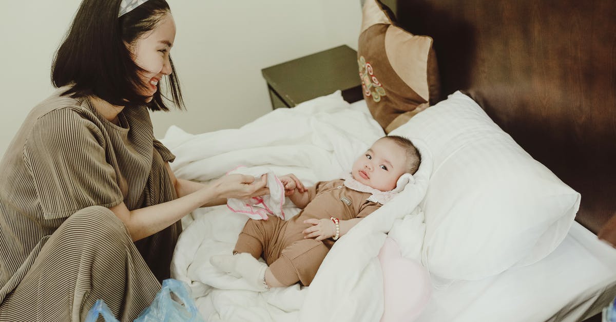 What is the reason to coddle an egg? - Young smiling Asian female mom in home clothes coddling with baby in bodysuit lying on white coverlet on bed What is the reason to coddle an egg? - Young smiling Asian female mom in home clothes coddling with baby in bodysuit lying on white coverlet on bed