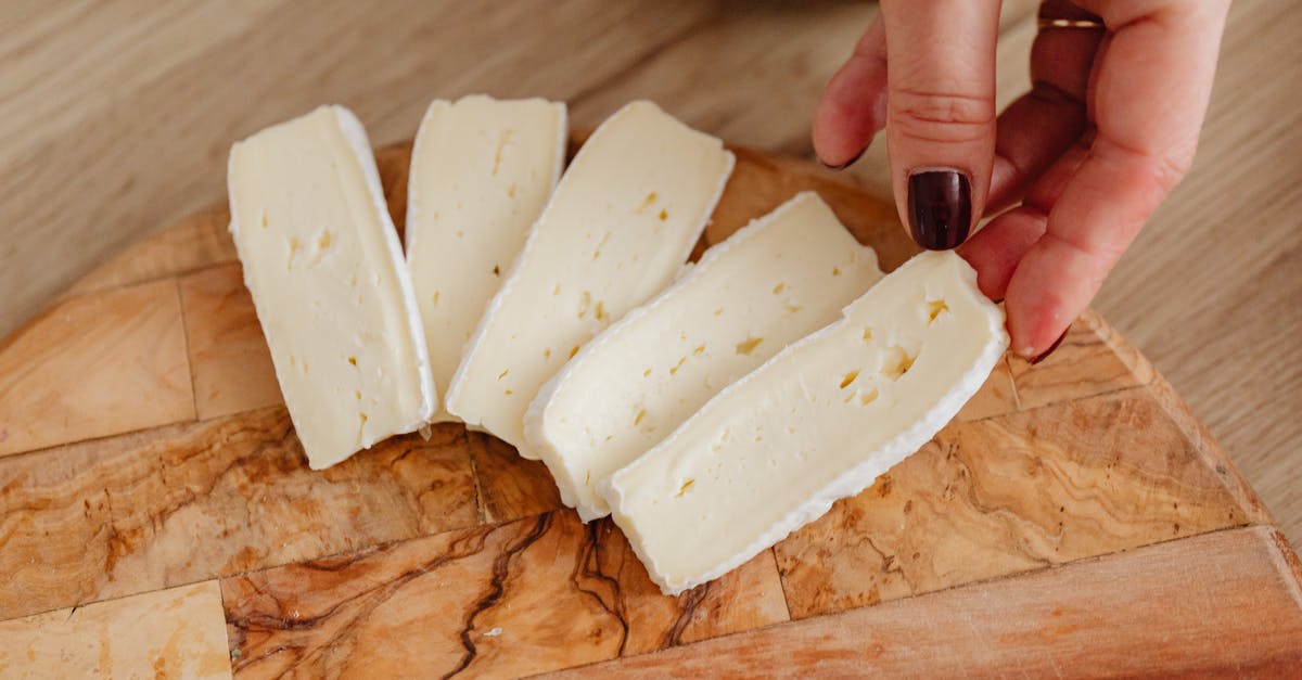 What is the rind of Brie cheese made of? - Person Holding White Cheese on Brown Wooden Chopping Board What is the rind of Brie cheese made of? - Person Holding White Cheese on Brown Wooden Chopping Board