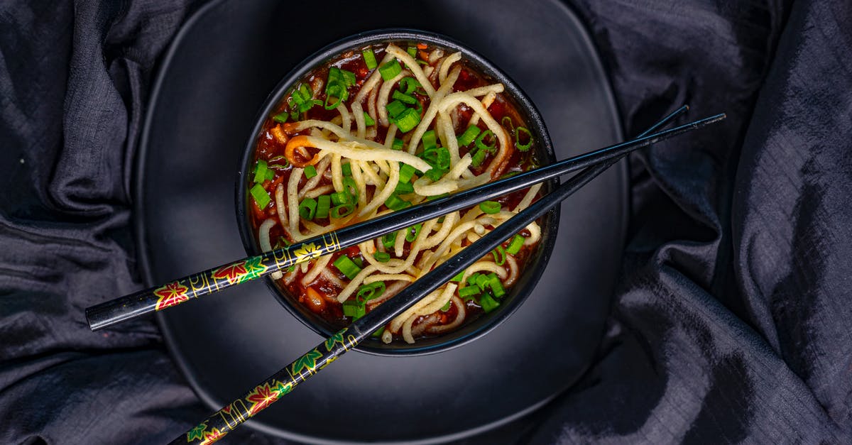 What is this Asian dish made with boiled vegetables? - Top view of black bowl with Asian soup with noodle and green onion served with bamboo chopsticks on black tablecloth What is this Asian dish made with boiled vegetables? - Top view of black bowl with Asian soup with noodle and green onion served with bamboo chopsticks on black tablecloth