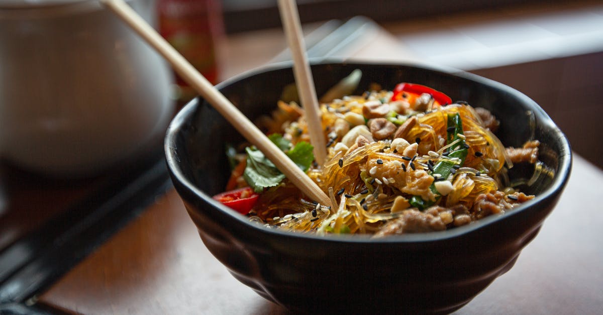 What is this Asian dish made with boiled vegetables? - Delicious appetizing Asian noodles with vegetables and nuts served in bowl with chopsticks on table What is this Asian dish made with boiled vegetables? - Delicious appetizing Asian noodles with vegetables and nuts served in bowl with chopsticks on table