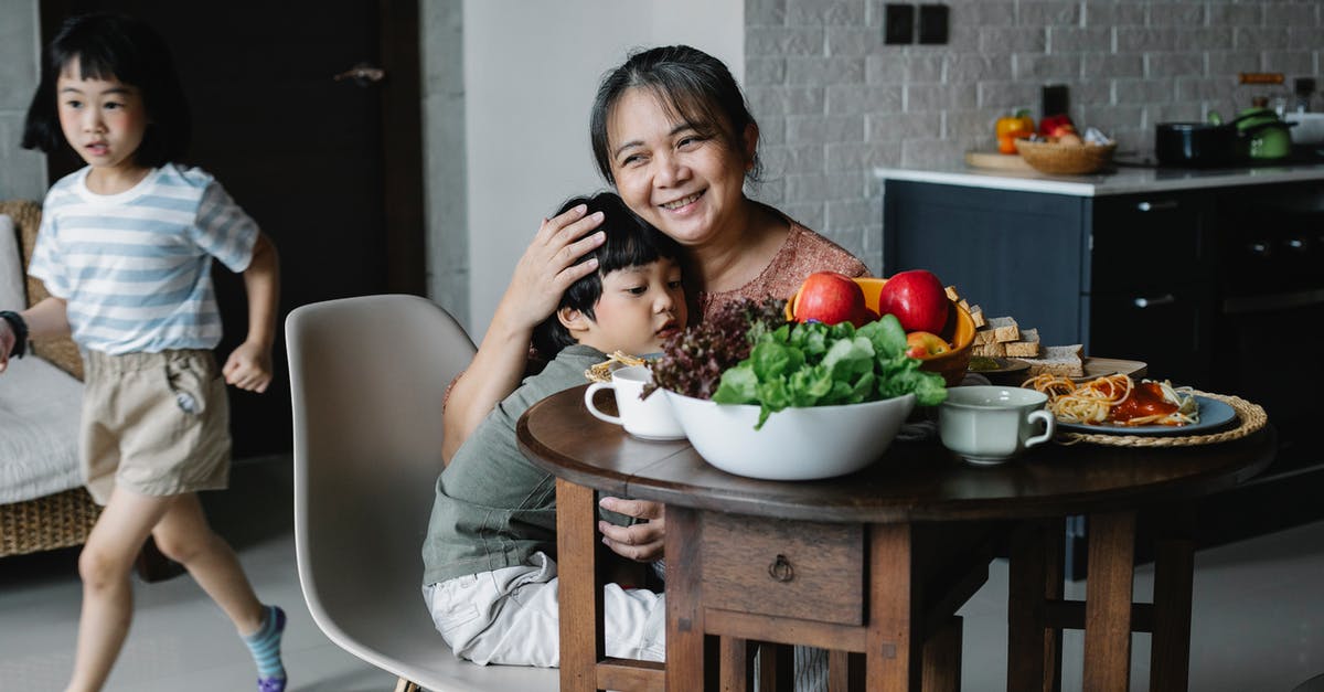 What kind of foods react with aluminium pressure cookers? - Happy kind ethnic senior female hugging cute grandson having breakfast in kitchen while active little granddaughter running behind table What kind of foods react with aluminium pressure cookers? - Happy kind ethnic senior female hugging cute grandson having breakfast in kitchen while active little granddaughter running behind table