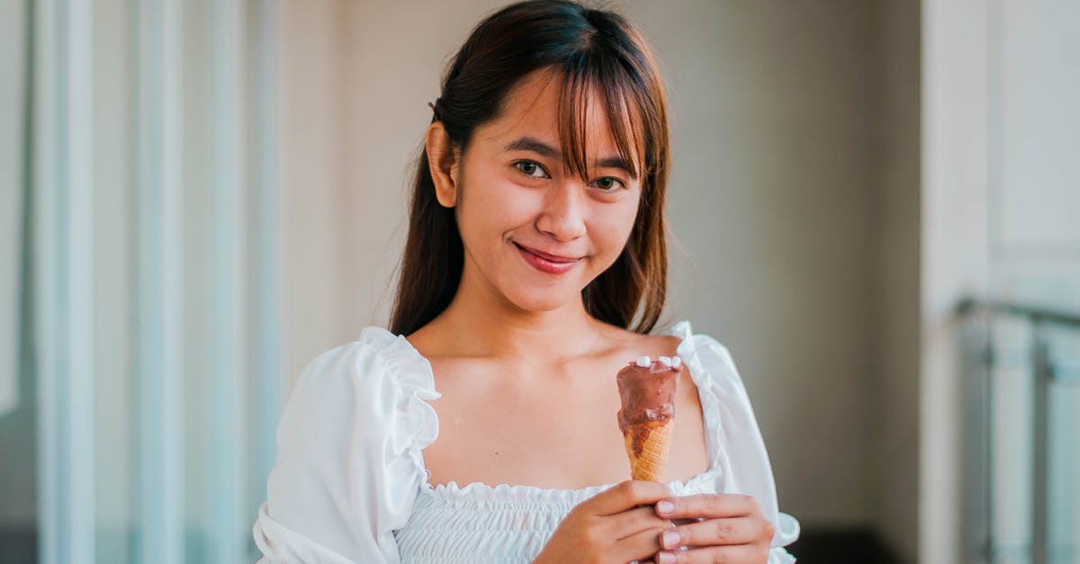 What non-dairy filler to use in white chocolate style coatings? - Cheerful Asian female in white outfit with sweet chocolate ice cream cone in hand looking at camera while standing on balcony What non-dairy filler to use in white chocolate style coatings? - Cheerful Asian female in white outfit with sweet chocolate ice cream cone in hand looking at camera while standing on balcony