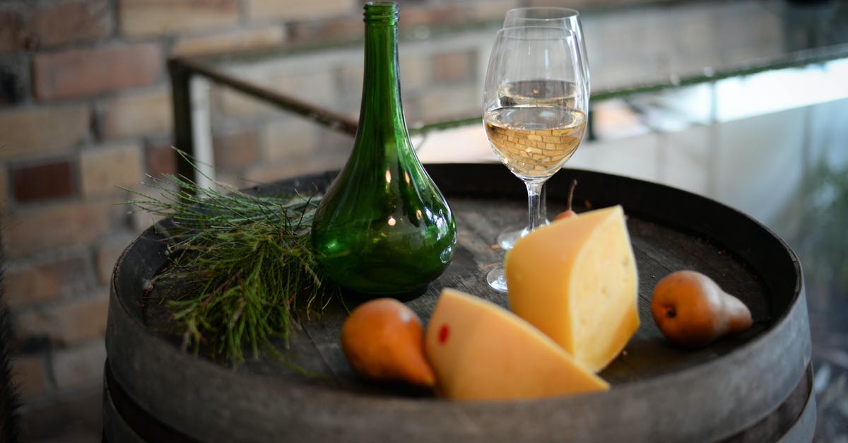 What role does alcoholic liquid play in cheese fondue recipes? - High angle of glass bottle with wineglasses placed on barrel with aromatic cheese and pears What role does alcoholic liquid play in cheese fondue recipes? - High angle of glass bottle with wineglasses placed on barrel with aromatic cheese and pears