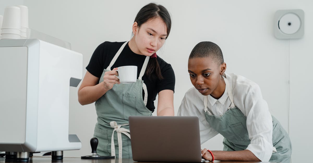 What special knowledge or skills about coffee do baristas have? - Serious Asian female barista with coffee in hand teaching new black colleague to use computer program while standing at table with laptop What special knowledge or skills about coffee do baristas have? - Serious Asian female barista with coffee in hand teaching new black colleague to use computer program while standing at table with laptop