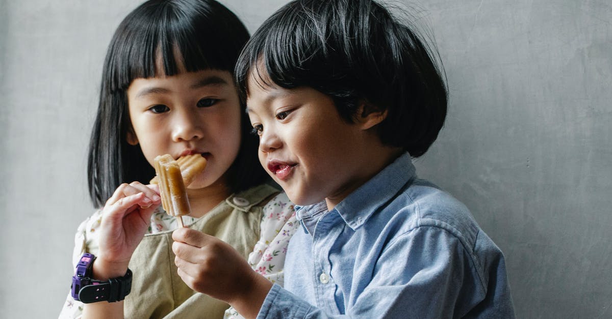 What style of icing is this please? - Adorable little Asian siblings with dark hair eating sweet yummy ice pop while standing near gray wall What style of icing is this please? - Adorable little Asian siblings with dark hair eating sweet yummy ice pop while standing near gray wall