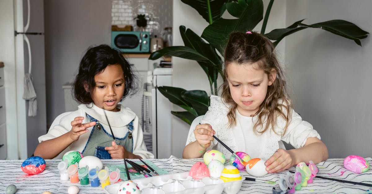 What temperatures should I keep my refrigerator and freezer set at? - Concentrated multiracial girls painting white eggs with paintbrushes while sitting at table with paints in kitchen during Easter holiday at home