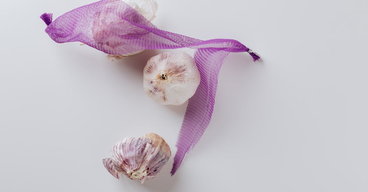 What turned my garlic purple? - Composition of garlic bulbs with purple net on white background What turned my garlic purple? - Composition of garlic bulbs with purple net on white background