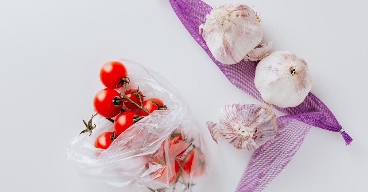 What turned my garlic purple? - Top view of fresh cherry tomatoes in transparent polyethylene bag and three heads of garlic placed on purple grid isolated on white background What turned my garlic purple? - Top view of fresh cherry tomatoes in transparent polyethylene bag and three heads of garlic placed on purple grid isolated on white background