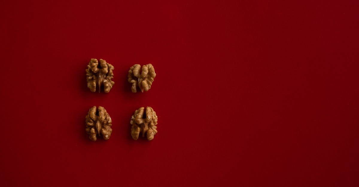What went wrong with my walnut brittle - Top view of halves of walnut kernel regularly placed on dark red background What went wrong with my walnut brittle - Top view of halves of walnut kernel regularly placed on dark red background