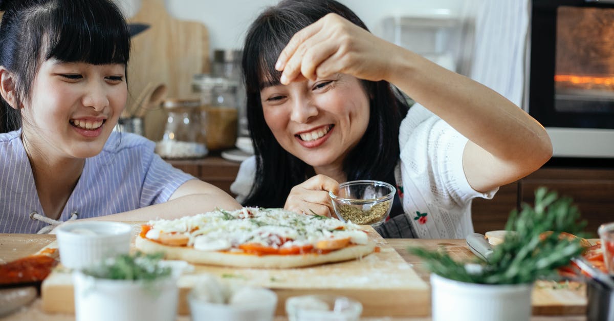 When should I add spinach to homemade pizza? - Cheerful Asian women sprinkling seasoning on pizza When should I add spinach to homemade pizza? - Cheerful Asian women sprinkling seasoning on pizza