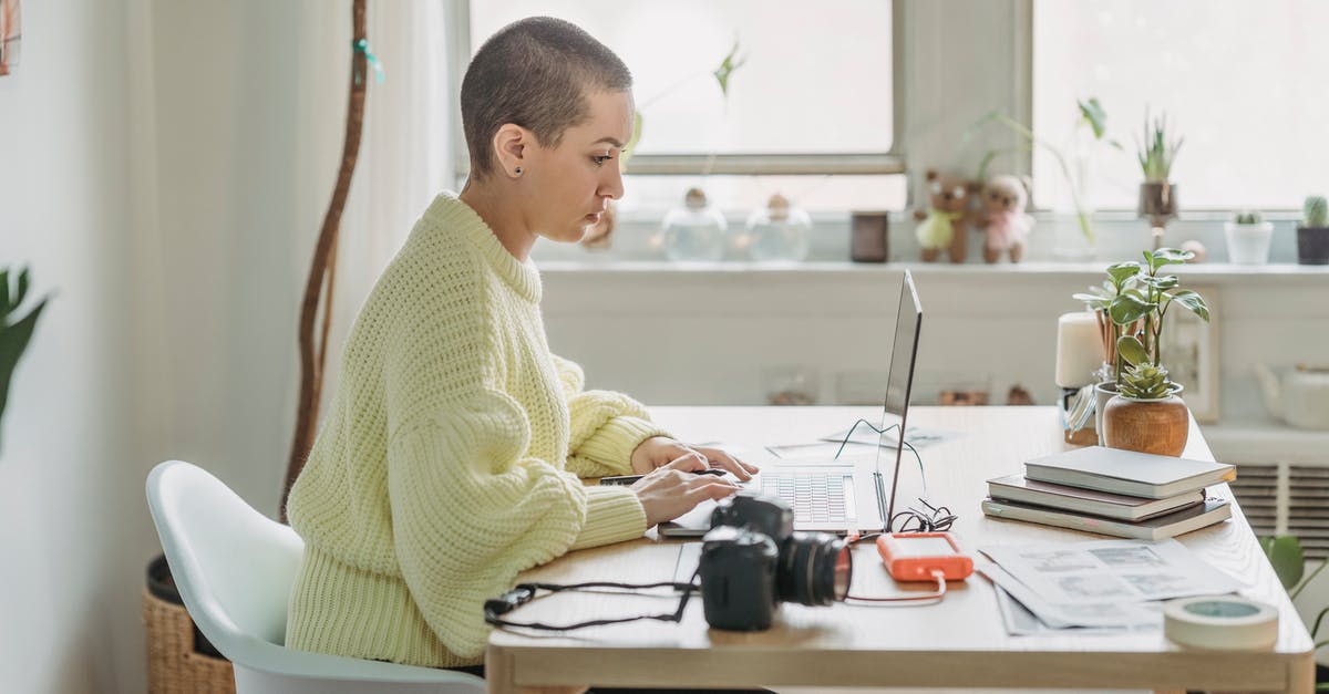 Which appliance to use for masala chai? - Side view of concentrated female with short hair editing photos on netbook while sitting at table with photo camera in light room