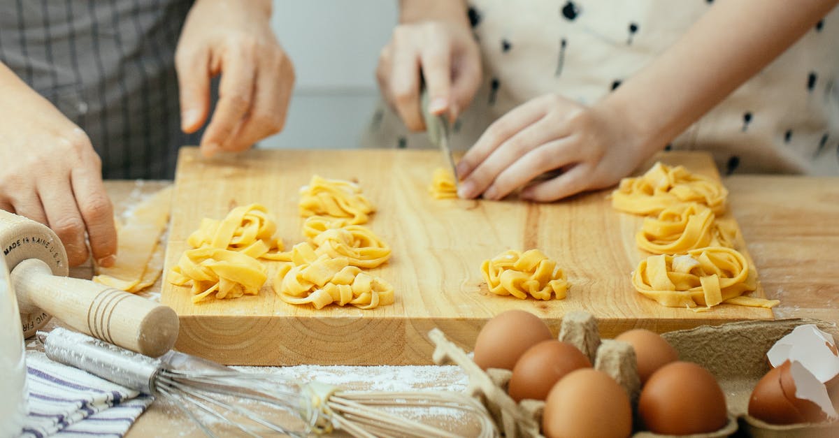 Which cut makes cheapest goulash? - Faceless females in aprons at wooden table making homemade pasta cutting dough into strips Which cut makes cheapest goulash? - Faceless females in aprons at wooden table making homemade pasta cutting dough into strips