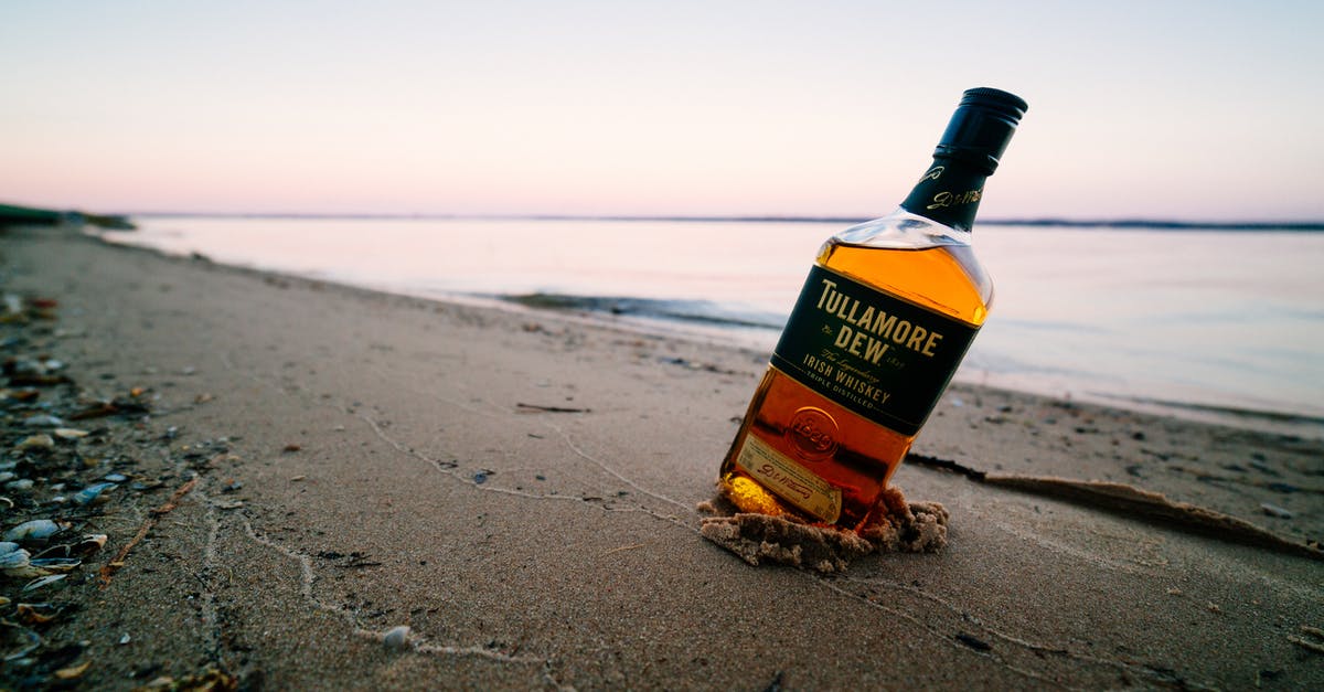 Whiskey and Water - Ground level of strong elite alcoholic drink in transparent glass bottle on wet sandy shore near calm endless ocean under sky at sunset Whiskey and Water - Ground level of strong elite alcoholic drink in transparent glass bottle on wet sandy shore near calm endless ocean under sky at sunset