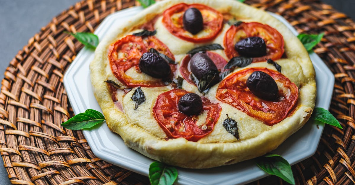 White dots on pizza or focaccia after baking - From above of tasty pizza with tomato and olive on plate with basil leaves White dots on pizza or focaccia after baking - From above of tasty pizza with tomato and olive on plate with basil leaves