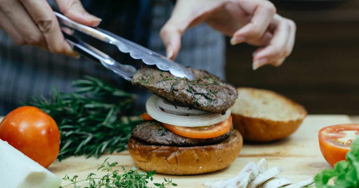 Why add malt to bread? - Unrecognizable female cook using tongs to put juicy meat on bun with onion and slice of tomato while making burger against blurred background Why add malt to bread? - Unrecognizable female cook using tongs to put juicy meat on bun with onion and slice of tomato while making burger against blurred background