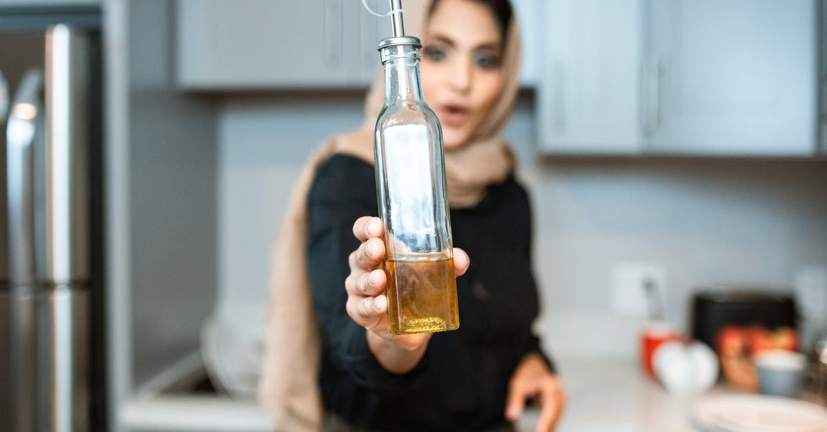 Why do chefs finish with olive oil? - Ethnic woman demonstrating bottle of olive oil while cooking Why do chefs finish with olive oil? - Ethnic woman demonstrating bottle of olive oil while cooking