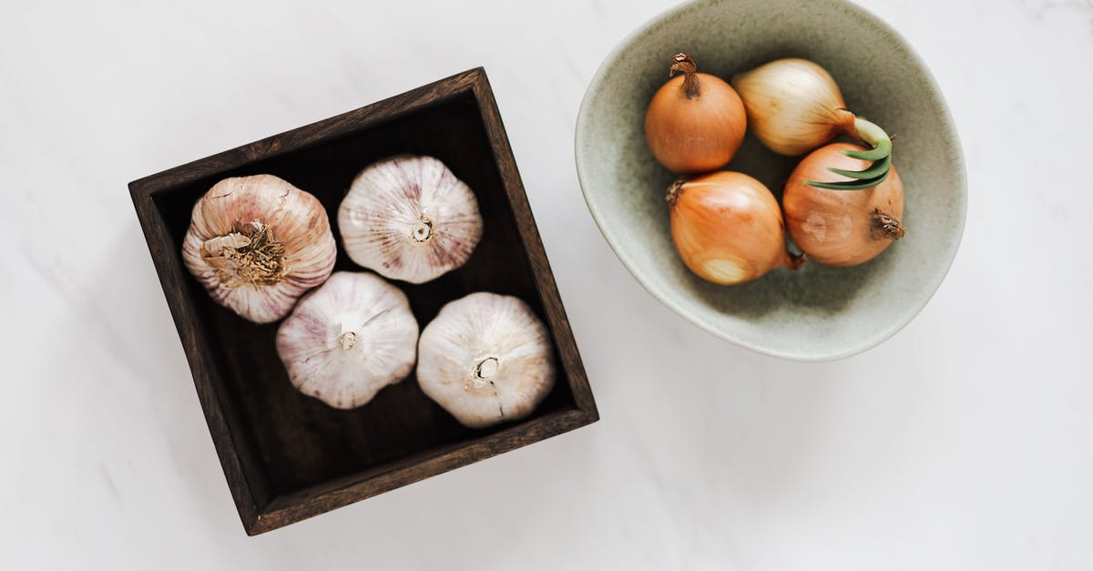 Why do garlic pots have holes? - Overhead of square pot with fresh unpeeled garlic near light green bowl with raw yellow onions against white marble surface Why do garlic pots have holes? - Overhead of square pot with fresh unpeeled garlic near light green bowl with raw yellow onions against white marble surface