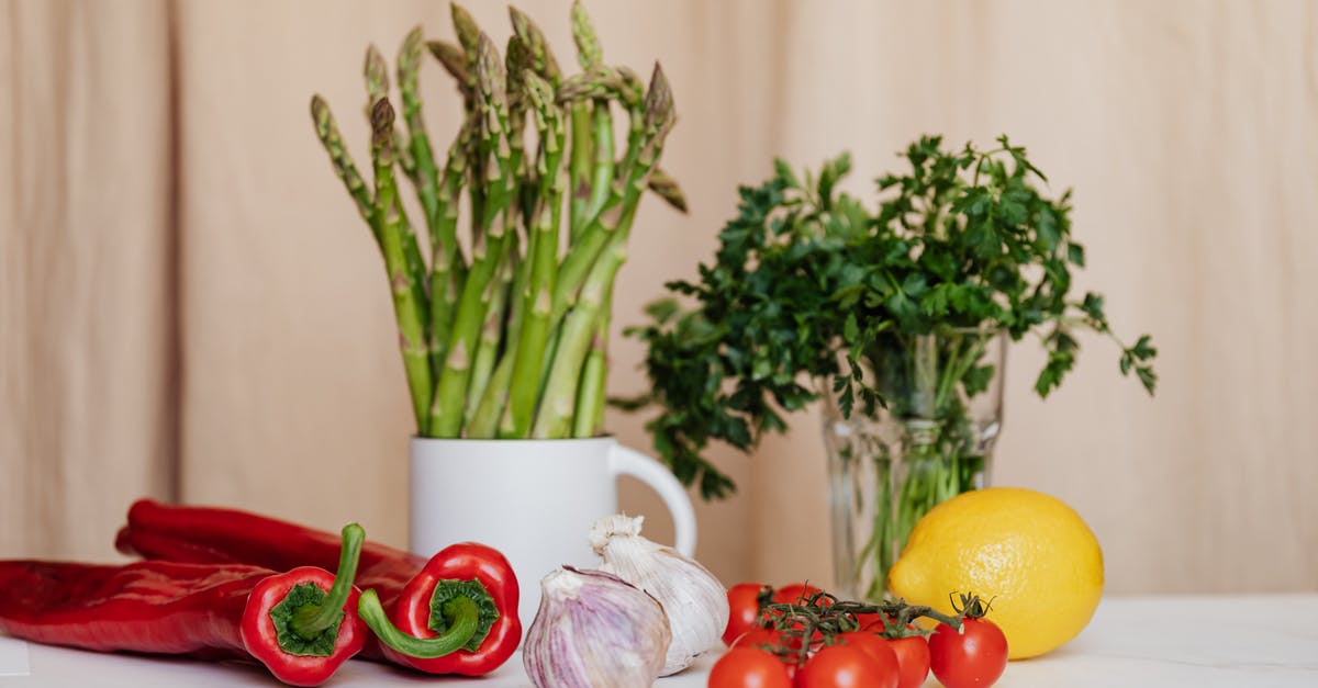 Why do we eat unripened chili peppers? - Composition of red cherry tomatoes and peppers with garlics and yellow lemon near white cup with asparagus and green parsley in glass on table Why do we eat unripened chili peppers? - Composition of red cherry tomatoes and peppers with garlics and yellow lemon near white cup with asparagus and green parsley in glass on table