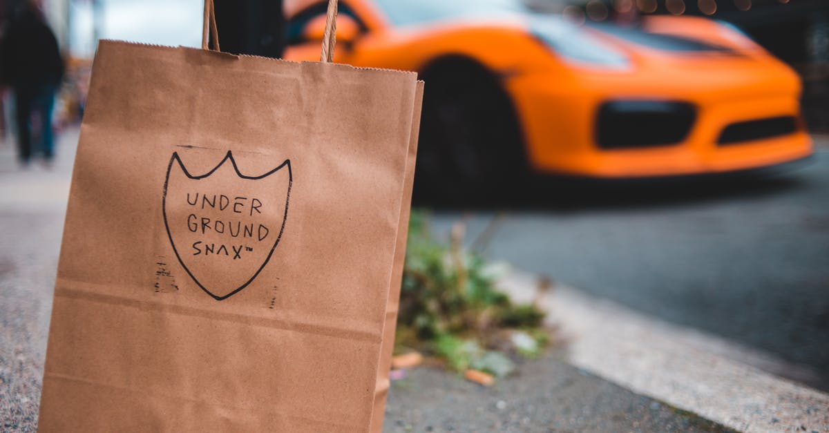 Why does a brown paper bag speed ripening? - Paper shopping bag with inscription placed on asphalt surface near road with driving modern orange sports car Why does a brown paper bag speed ripening? - Paper shopping bag with inscription placed on asphalt surface near road with driving modern orange sports car